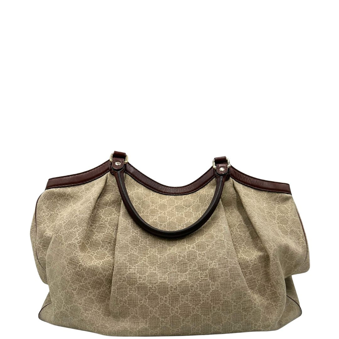 Retro di una borsa Gucci Sukey in tessuto beige GG con finiture in pelle marrone mogano, doppi manici stondati e ciondolo con doppie G incrociate. Rifinita con parti metalliche dorate. Indossabile a spalla.