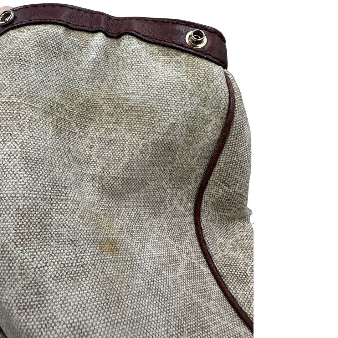 Laterale di una borsa Gucci Sukey in tessuto beige GG con finiture in pelle marrone mogano, doppi manici stondati e ciondolo con doppie G incrociate. Rifinita con parti metalliche dorate. Indossabile a spalla.