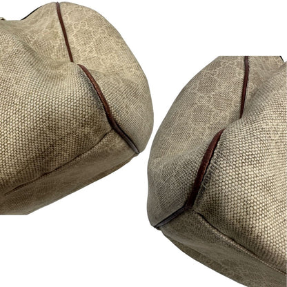Angoli di una borsa Gucci Sukey in tessuto beige GG con finiture in pelle marrone mogano, doppi manici stondati e ciondolo con doppie G incrociate. Rifinita con parti metalliche dorate. Indossabile a spalla.