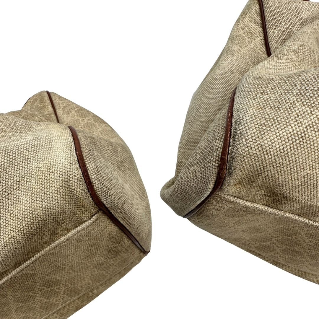 Angoli di una borsa Gucci Sukey in tessuto beige GG con finiture in pelle marrone mogano, doppi manici stondati e ciondolo con doppie G incrociate. Rifinita con parti metalliche dorate. Indossabile a spalla.