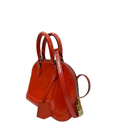 lato Borsa Louis Vuitton Alma BB in pelle Vernis arancione corallo monogram e parti metalliche dorate. Munita di doppi manici stondati e una tracolla amovibile, dotata di clochette porta chiavi. Completa di dustbag, lucchetto e chiavi, di lusso, originale, ottime condizioni, usata. 
