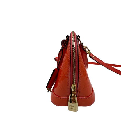 lato Borsa Louis Vuitton Alma BB in pelle Vernis arancione corallo monogram e parti metalliche dorate. Munita di doppi manici stondati e una tracolla amovibile, dotata di clochette porta chiavi. Completa di dustbag, lucchetto e chiavi, di lusso, originale, ottime condizioni, usata. 