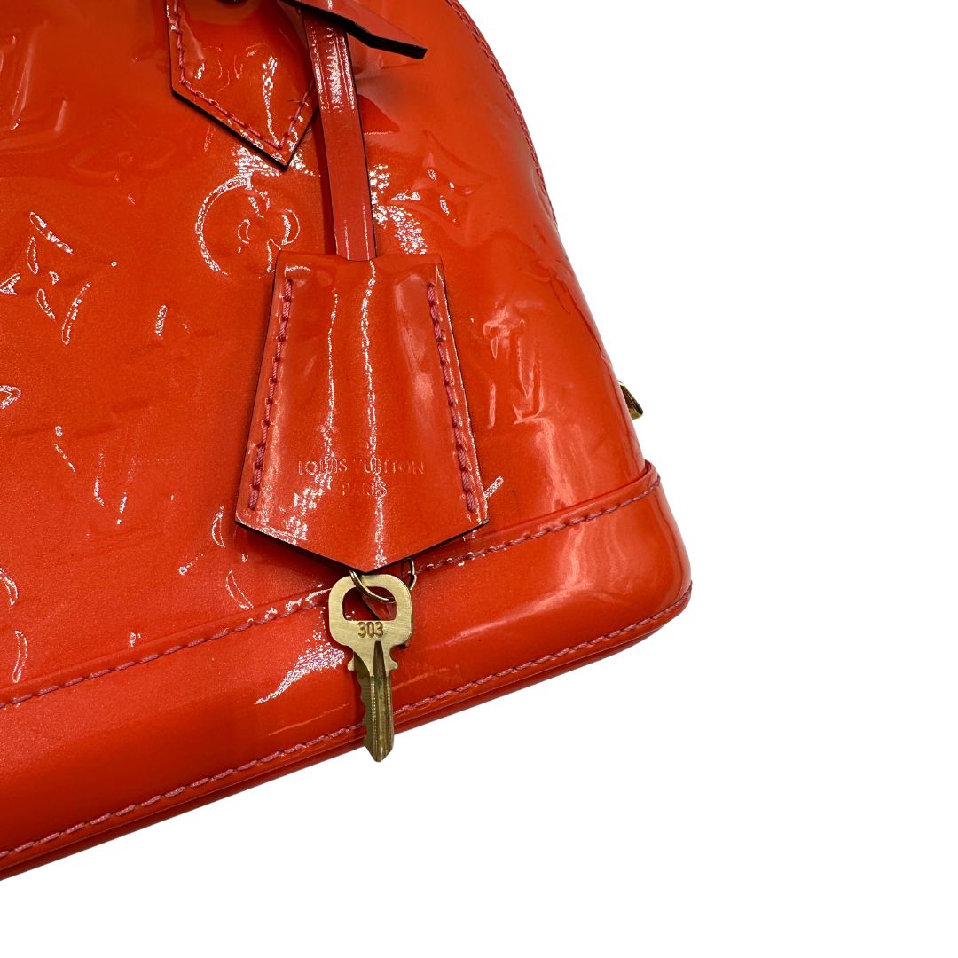 clochette Borsa Louis Vuitton Alma BB in pelle Vernis arancione corallo monogram e parti metalliche dorate. Munita di doppi manici stondati e una tracolla amovibile, dotata di clochette porta chiavi. Completa di dustbag, lucchetto e chiavi, di lusso, originale, ottime condizioni, usata. 