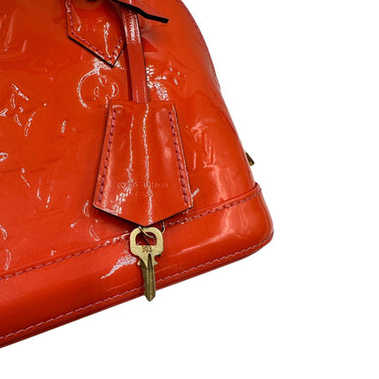 clochette Borsa Louis Vuitton Alma BB in pelle Vernis arancione corallo monogram e parti metalliche dorate. Munita di doppi manici stondati e una tracolla amovibile, dotata di clochette porta chiavi. Completa di dustbag, lucchetto e chiavi, di lusso, originale, ottime condizioni, usata. 