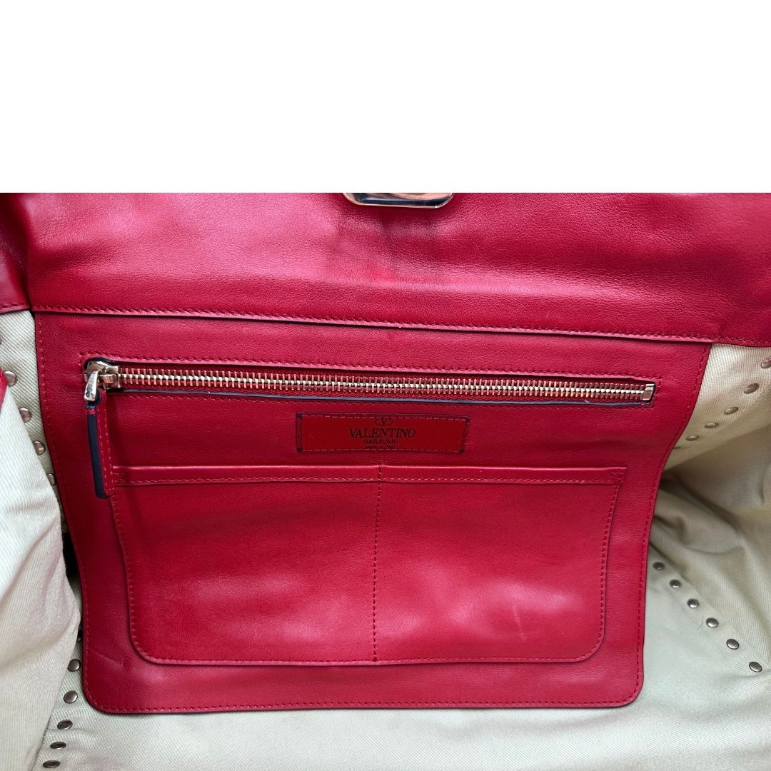 Interno di una borsa Valentino Garavani in pelle rossa con parti metalliche dorate; impreziosita da borchie piramidali e munita di doppi manici e tracolla amovibile. Completa di dustbag. 