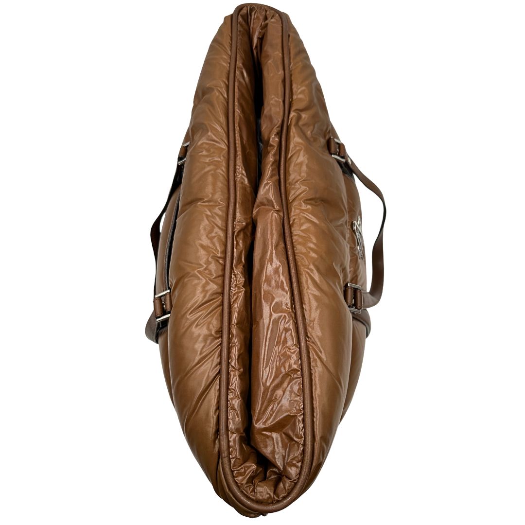 Vista superiore di una borsa Moncler in poliuretano color caramello effetto imbottito e finiture in pelle tono su tono, con metalleria dorata. Munita di cartellino. Da indossare a spalla.