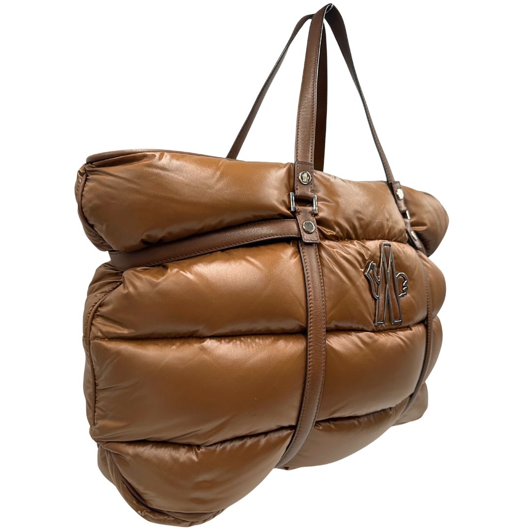 Laterale sinistro di una borsa Moncler in poliuretano color caramello effetto imbottito e finiture in pelle tono su tono, con metalleria dorata. Munita di cartellino. Da indossare a spalla.