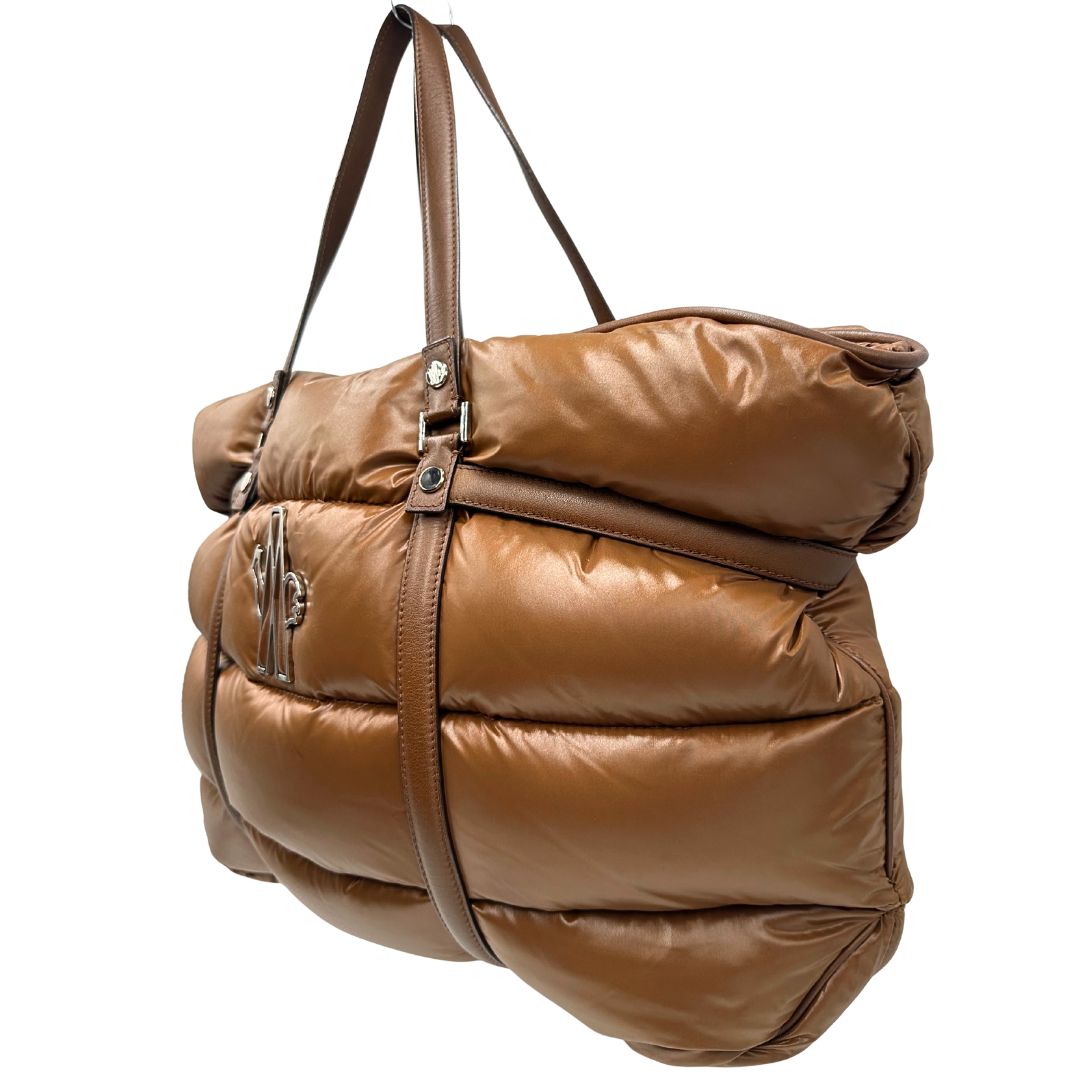 Laterale destro di una borsa Moncler in poliuretano color caramello effetto imbottito e finiture in pelle tono su tono, con metalleria dorata. Munita di cartellino. Da indossare a spalla.