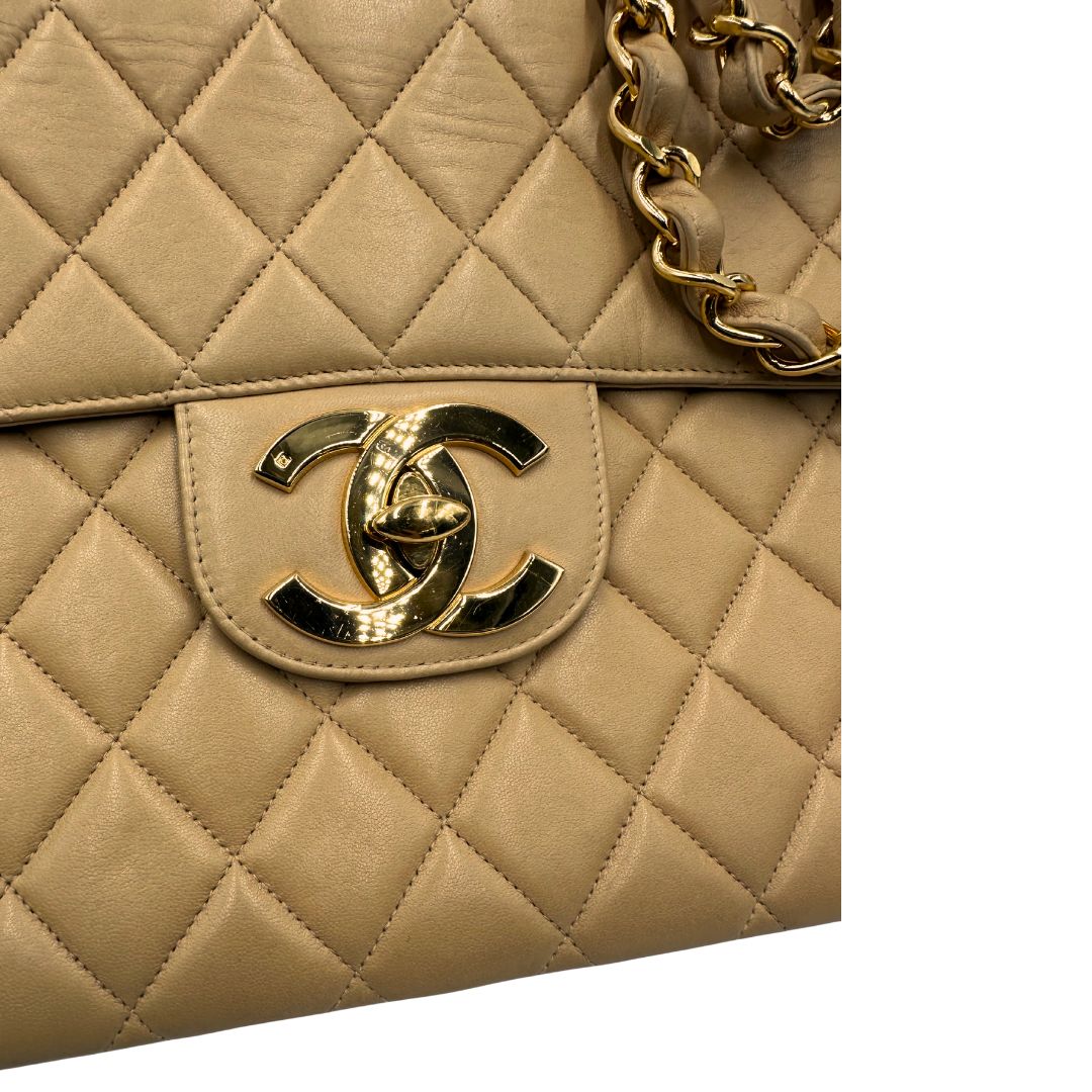 Logo metallico di una borsa Chanel in pelle beige matelassè e parti metalliche dorate; munita di una tracolla scorrevole in catena e pelle. Indossabile a spalla e a tracolla. Completa di scatola, dustbag e card d'autenticità.