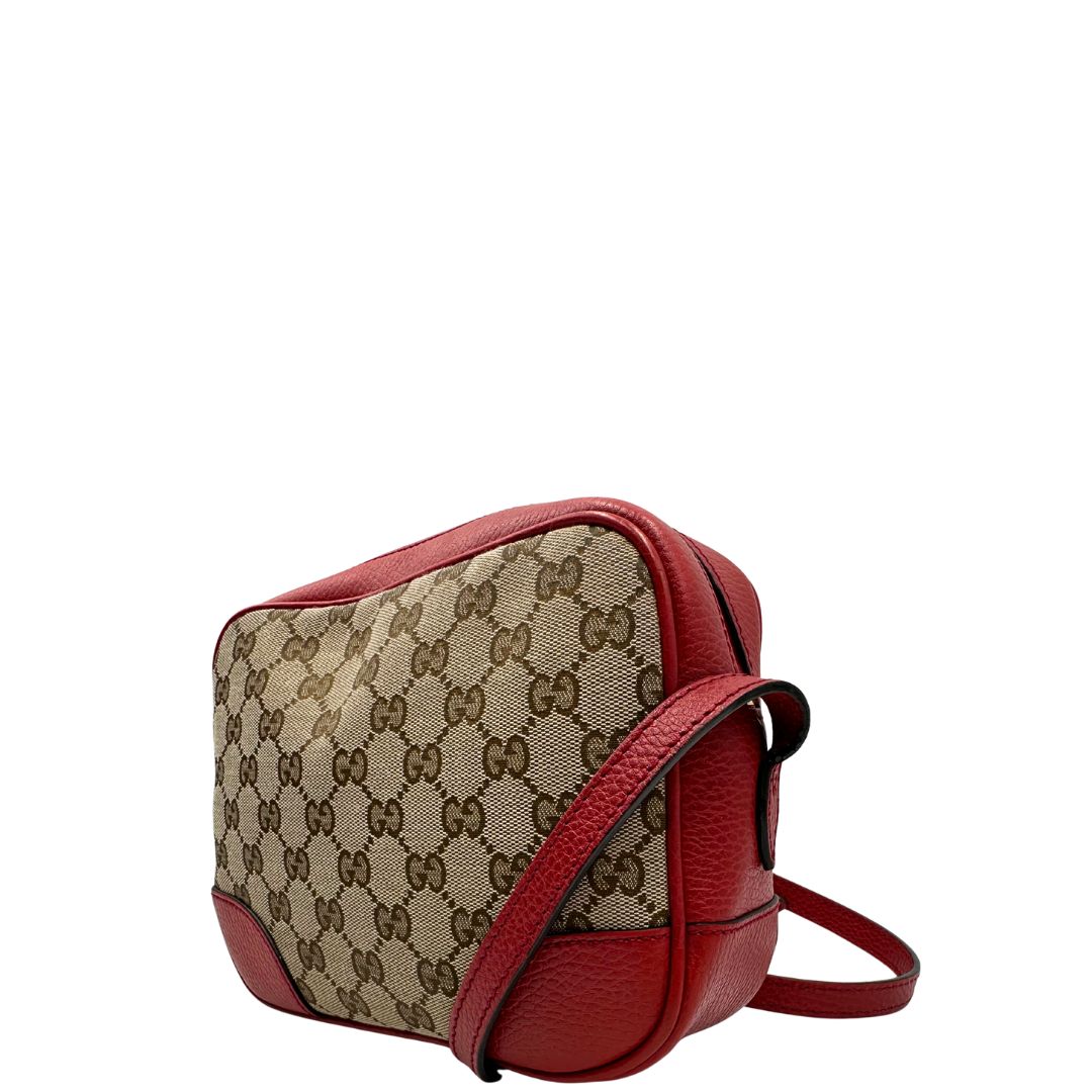 Lato sinistro di una Borsa Gucci in tessuto GG beige con finiture in pelle martellata rossa e parti metalliche dorate; munita di una tracoll regolabile. Completa di dustbag. Originale, usata, di lusso, in ottime condizioni.