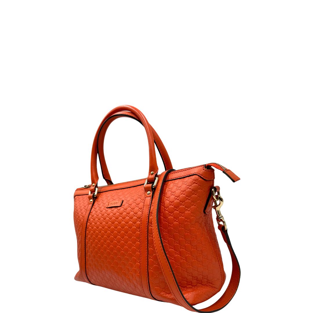Laterale destro di una borsa Gucci in pelle arancione GG con parti metalliche dorate; munita di doppi manici e una tracolla amovibile e regolabile.