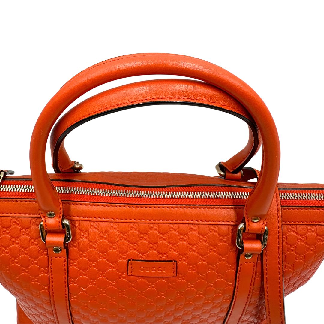 Manici di una borsa Gucci in pelle arancione GG con parti metalliche dorate; munita di doppi manici e una tracolla amovibile e regolabile.