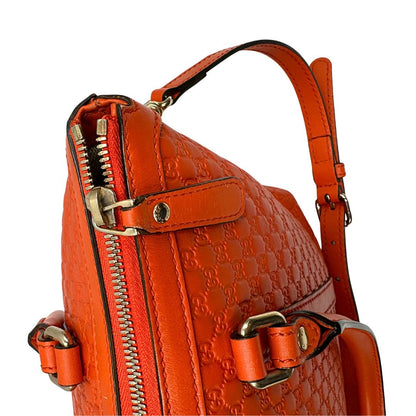 Dettaglio cerniera di una borsa Gucci in pelle arancione GG con parti metalliche dorate; munita di doppi manici e una tracolla amovibile e regolabile.