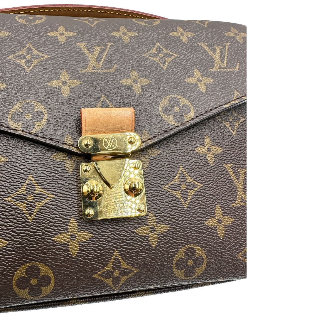 Chiusura di una borsa Louis Vuitton Métis in canvas marrone monogram con dettagli in vacchetta naturale e parti metalliche dorate. Munita di un manico singolo e una tracolla regolabile e amovibile. Dotata di scatola.