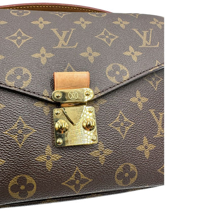 Chiusura di una borsa Louis Vuitton Métis in canvas marrone monogram con dettagli in vacchetta naturale e parti metalliche dorate. Munita di un manico singolo e una tracolla regolabile e amovibile. Dotata di scatola.