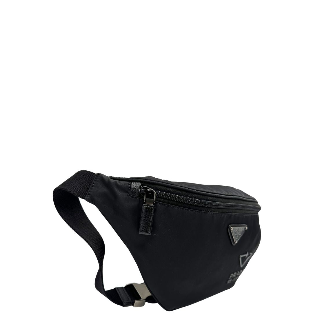 Laterale sinistro di un marsupio Prada in Re-Nylon nero con dettagli in pelle tono su tono, logo gommato sul front e parti in metallo argentato. Leggermente regolabile, indossabile a marsupio o cross body.
