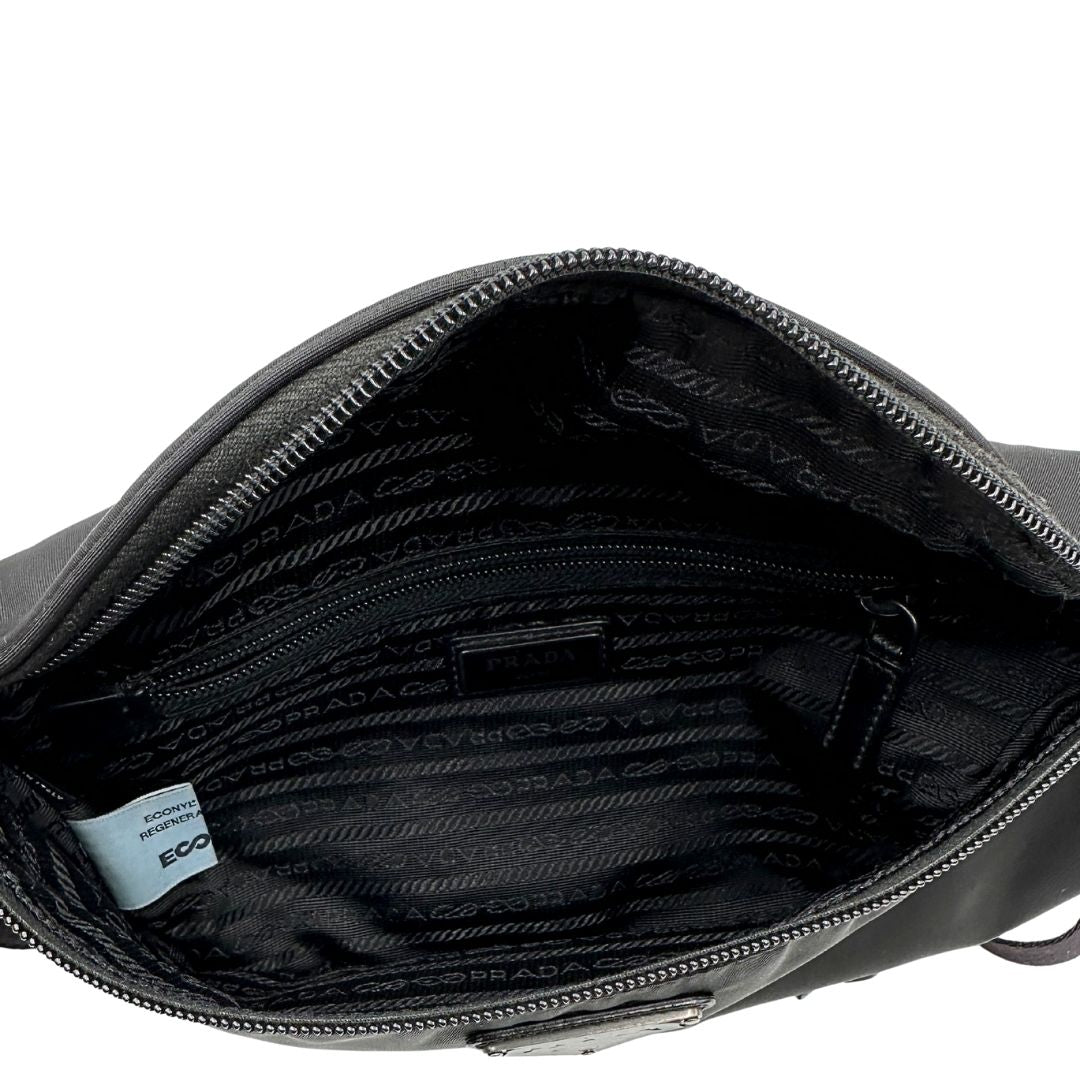 Interno di un marsupio Prada in Re-Nylon nero con dettagli in pelle tono su tono, logo gommato sul front e parti in metallo argentato. Leggermente regolabile, indossabile a marsupio o cross body.