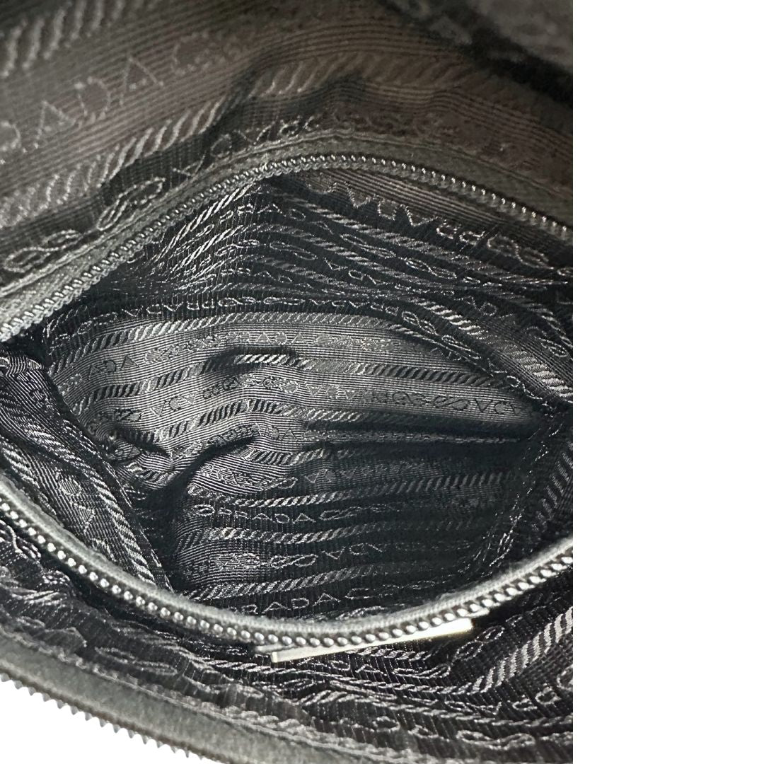 Interno di un marsupio Prada in Re-Nylon nero con dettagli in pelle tono su tono, logo gommato sul front e parti in metallo argentato. Leggermente regolabile, indossabile a marsupio o cross body.