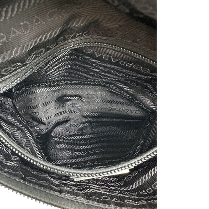 Interno di un marsupio Prada in Re-Nylon nero con dettagli in pelle tono su tono, logo gommato sul front e parti in metallo argentato. Leggermente regolabile, indossabile a marsupio o cross body.