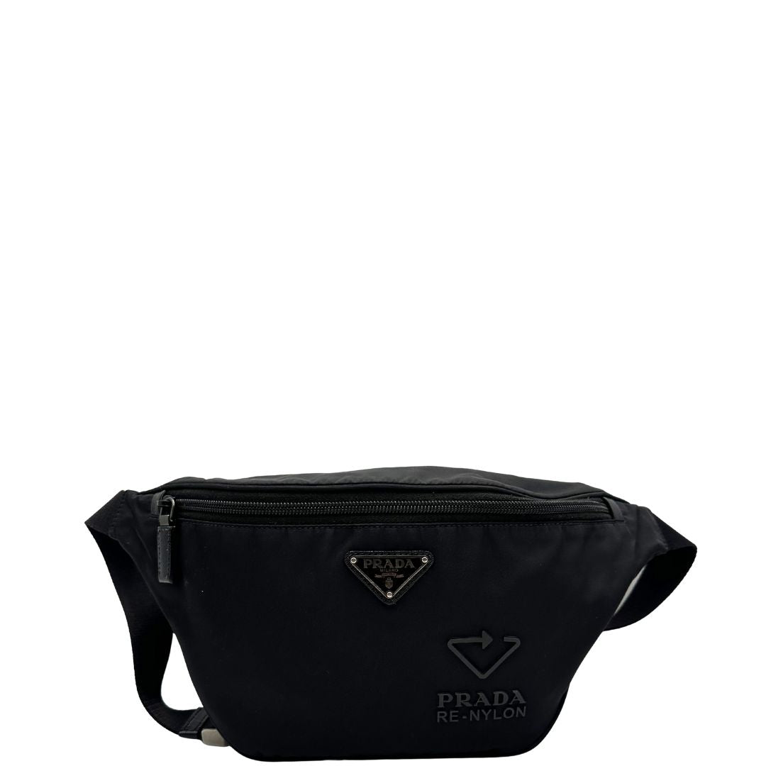 Front di un marsupio Prada in Re-Nylon nero con dettagli in pelle tono su tono, logo gommato sul front e parti in metallo argentato. Leggermente regolabile, indossabile a marsupio o cross body.