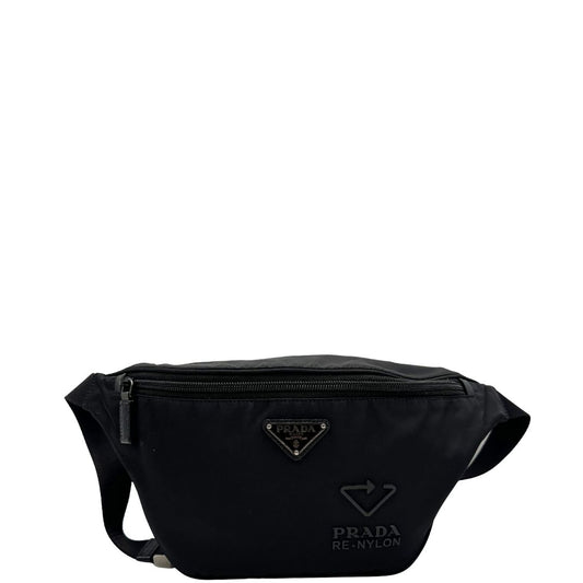 Front di un marsupio Prada in Re-Nylon nero con dettagli in pelle tono su tono, logo gommato sul front e parti in metallo argentato. Leggermente regolabile, indossabile a marsupio o cross body.