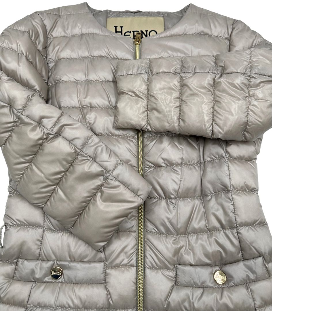 Piumino Herno in 100% poliammide color champagne. Maniche a 3/4 e parti metalliche dorate.
