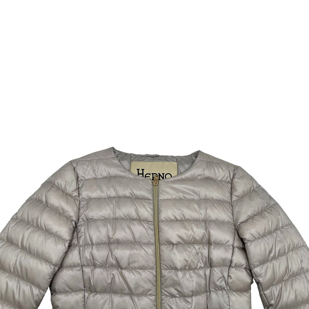 Piumino Herno in 100% poliammide color champagne. Maniche a 3/4 e parti metalliche dorate.