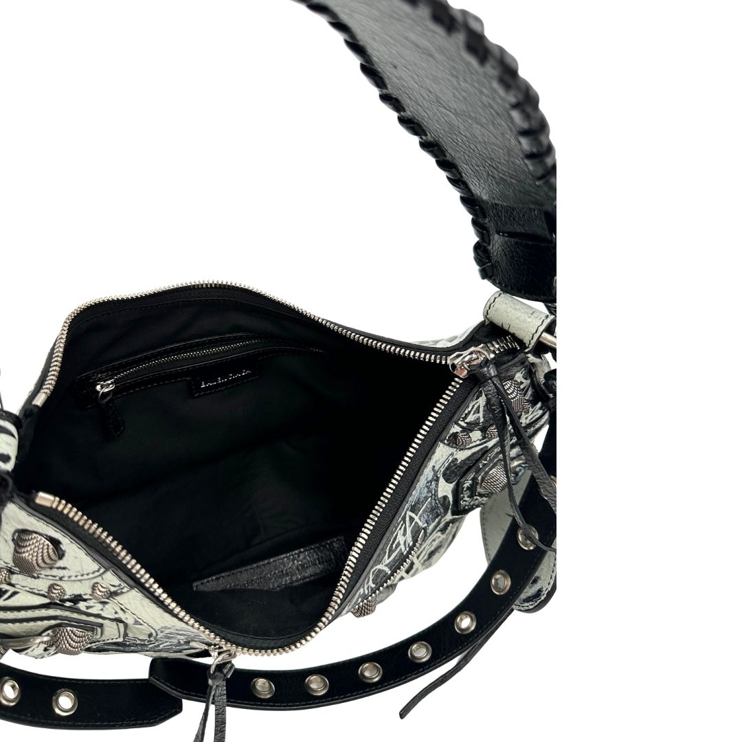 Interno di una borsa Balenciaga Le Cagole Graffiti in pelle nera con stampa graffiti color menta ghiacciata; dotata di manico leggermente regolabile con spallaccio. Pati metalliche argento anticato. Presenta tasca frontale con zip, lacci pendenti e ciondolo a cuore con specchietto integrato. Munita di scatola e dustbag. Indossabile a spalla.
