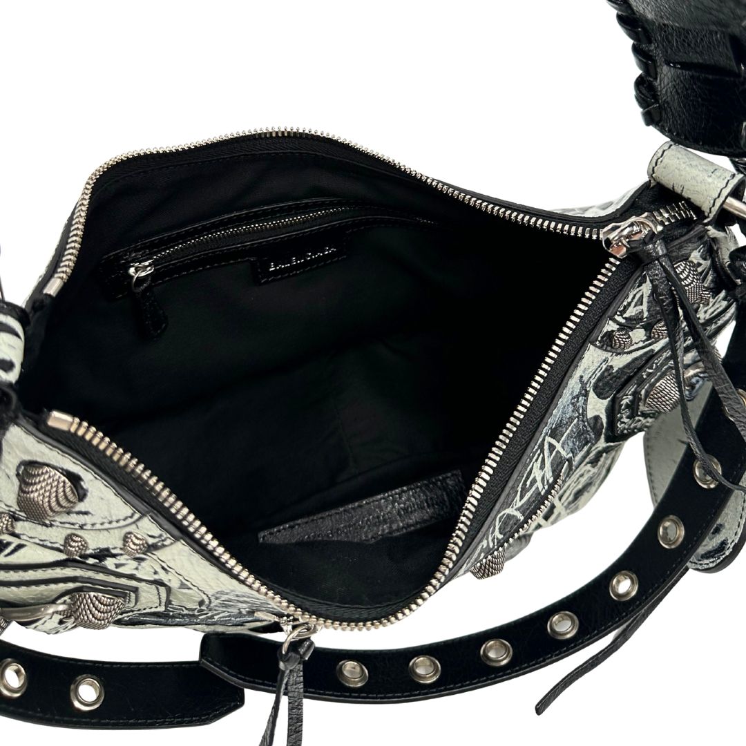 Interno di una borsa Balenciaga Le Cagole Graffiti in pelle nera con stampa graffiti color menta ghiacciata; dotata di manico leggermente regolabile con spallaccio. Pati metalliche argento anticato. Presenta tasca frontale con zip, lacci pendenti e ciondolo a cuore con specchietto integrato. Munita di scatola e dustbag. Indossabile a spalla.