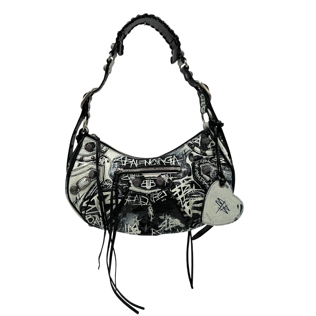 Front di una borsa Balenciaga Le Cagole Graffiti in pelle nera con stampa graffiti color menta ghiacciata; dotata di manico leggermente regolabile con spallaccio. Pati metalliche argento anticato. Presenta tasca frontale con zip, lacci pendenti e ciondolo a cuore con specchietto integrato. Munita di scatola e dustbag. Indossabile a spalla.