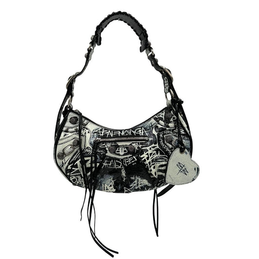 Front di una borsa Balenciaga Le Cagole Graffiti in pelle nera con stampa graffiti color menta ghiacciata; dotata di manico leggermente regolabile con spallaccio. Pati metalliche argento anticato. Presenta tasca frontale con zip, lacci pendenti e ciondolo a cuore con specchietto integrato. Munita di scatola e dustbag. Indossabile a spalla.