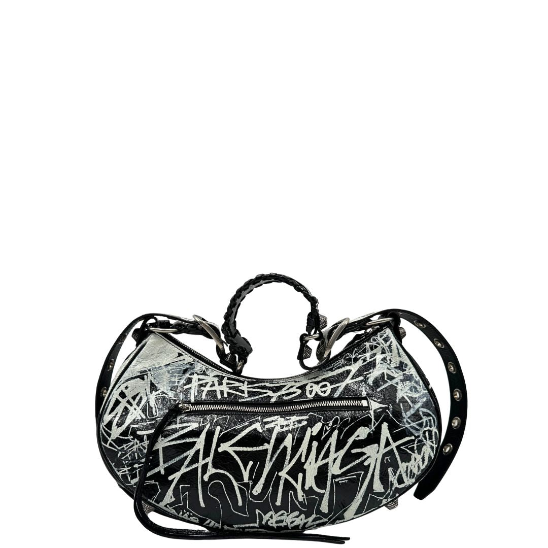 Retro di una borsa Balenciaga Le Cagole Graffiti in pelle nera con stampa graffiti color menta ghiacciata; dotata di manico leggermente regolabile con spallaccio. Pati metalliche argento anticato. Presenta tasca frontale con zip, lacci pendenti e ciondolo a cuore con specchietto integrato. Munita di scatola e dustbag. Indossabile a spalla.