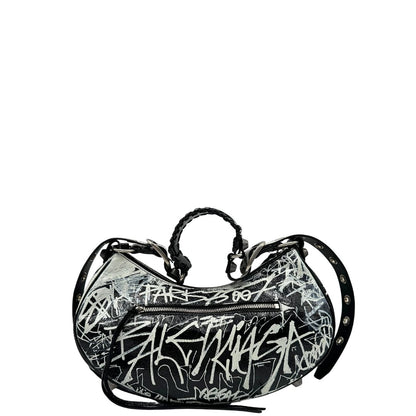 Retro di una borsa Balenciaga Le Cagole Graffiti in pelle nera con stampa graffiti color menta ghiacciata; dotata di manico leggermente regolabile con spallaccio. Pati metalliche argento anticato. Presenta tasca frontale con zip, lacci pendenti e ciondolo a cuore con specchietto integrato. Munita di scatola e dustbag. Indossabile a spalla.