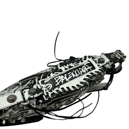 Vista superiore di una borsa Balenciaga Le Cagole Graffiti in pelle nera con stampa graffiti color menta ghiacciata; dotata di manico leggermente regolabile con spallaccio. Pati metalliche argento anticato. Presenta tasca frontale con zip, lacci pendenti e ciondolo a cuore con specchietto integrato. Munita di scatola e dustbag. Indossabile a spalla.