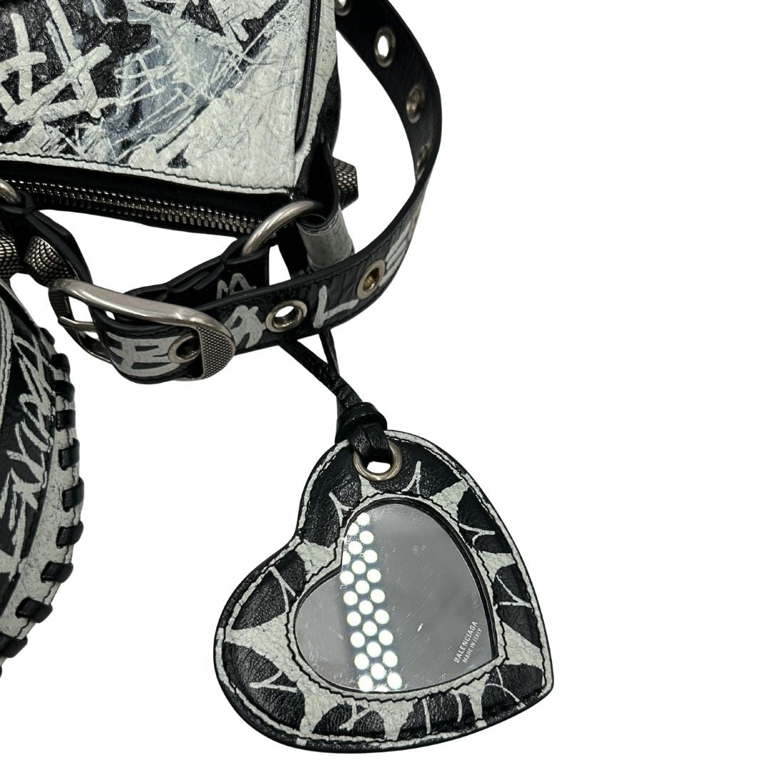 Specchietto di una borsa Balenciaga Le Cagole Graffiti in pelle nera con stampa graffiti color menta ghiacciata; dotata di manico leggermente regolabile con spallaccio. Pati metalliche argento anticato. Presenta tasca frontale con zip, lacci pendenti e ciondolo a cuore con specchietto integrato. Munita di scatola e dustbag. Indossabile a spalla.