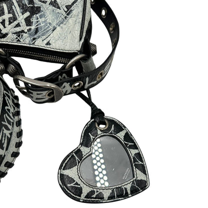 Specchietto di una borsa Balenciaga Le Cagole Graffiti in pelle nera con stampa graffiti color menta ghiacciata; dotata di manico leggermente regolabile con spallaccio. Pati metalliche argento anticato. Presenta tasca frontale con zip, lacci pendenti e ciondolo a cuore con specchietto integrato. Munita di scatola e dustbag. Indossabile a spalla.