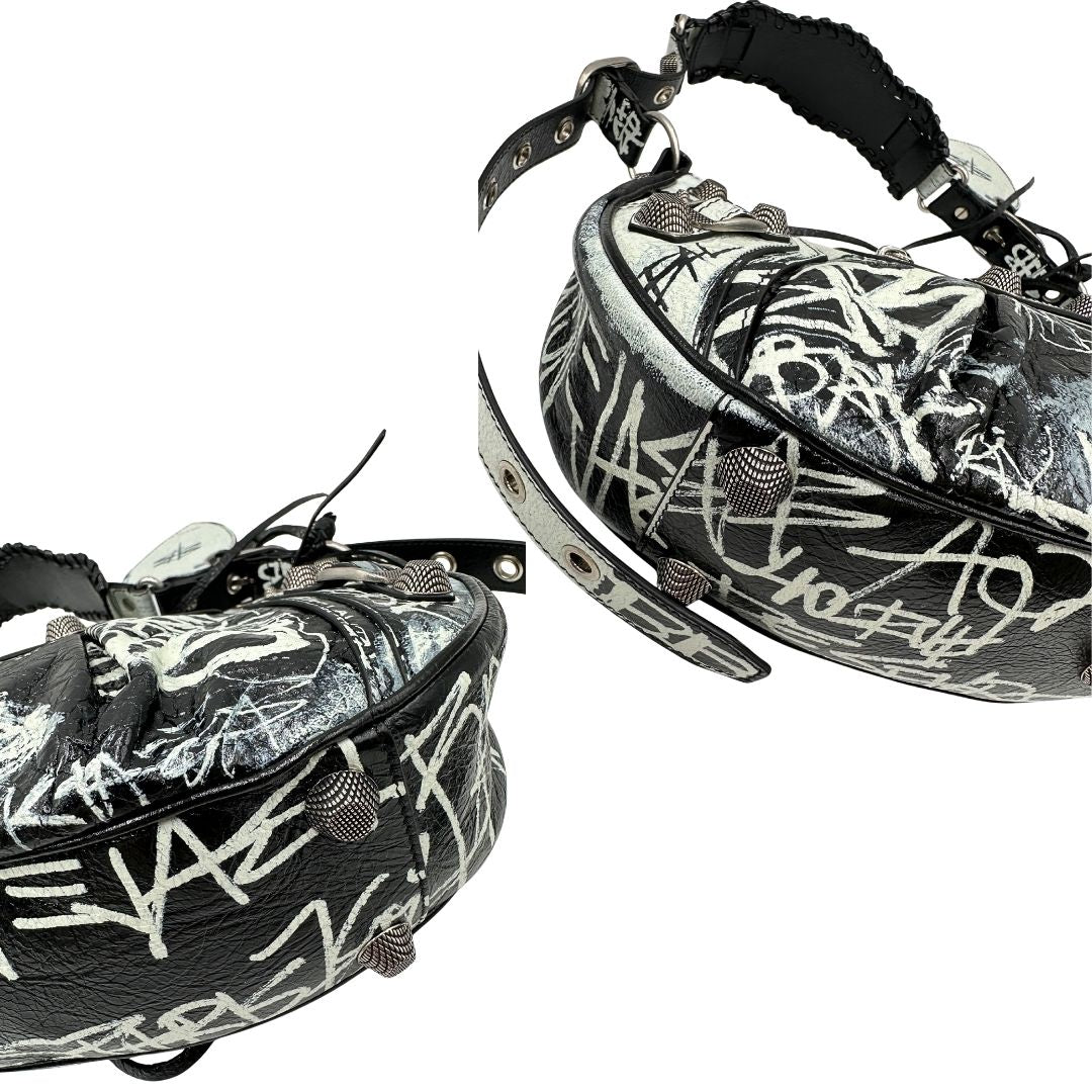 Angoli di una borsa Balenciaga Le Cagole Graffiti in pelle nera con stampa graffiti color menta ghiacciata; dotata di manico leggermente regolabile con spallaccio. Pati metalliche argento anticato. Presenta tasca frontale con zip, lacci pendenti e ciondolo a cuore con specchietto integrato. Munita di scatola e dustbag. Indossabile a spalla.