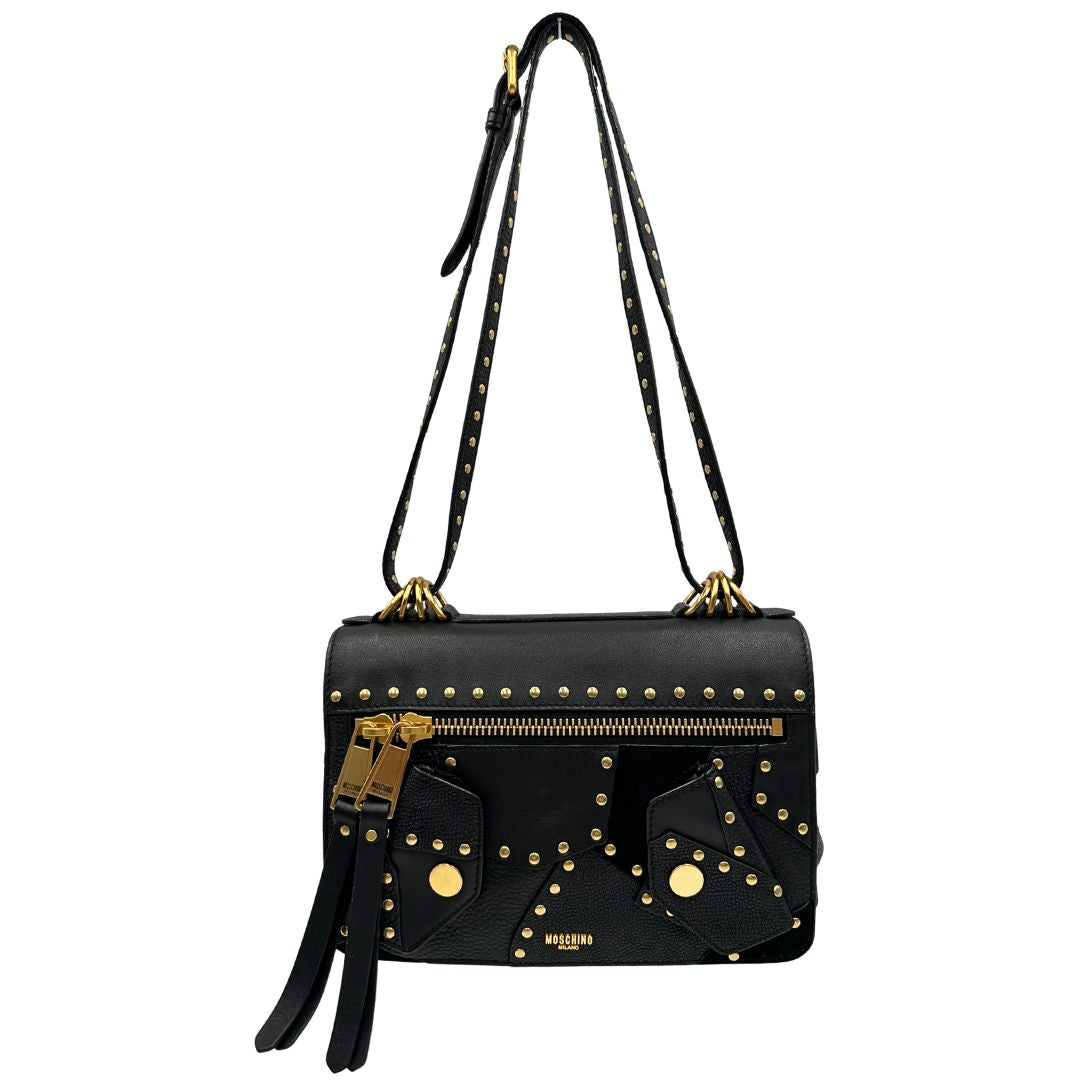 Front di una Borsa Moschino in pelle nera con inserti metallici dorati, arricchita da borchie dorate, zip frontale con maxi tirazip e applicazioni geometriche. munita di una tracolla regolabile non amovibile. Completa di Card d'autenticità Misure. Originale, Usata, di lusso, in ottime condizioni.