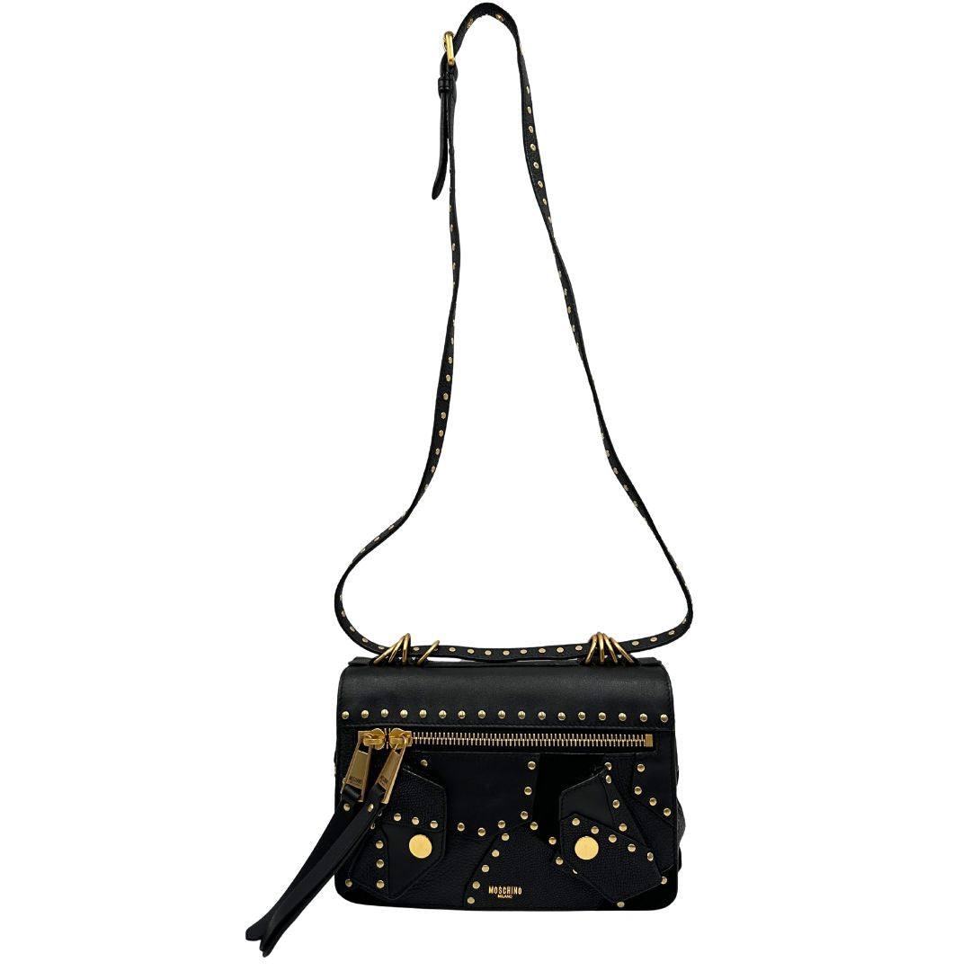 Front di una Borsa Moschino in pelle nera con inserti metallici dorati, arricchita da borchie dorate, zip frontale con maxi tirazip e applicazioni geometriche. munita di una tracolla regolabile non amovibile. Completa di Card d'autenticità Misure. Originale, Usata, di lusso, in ottime condizioni.