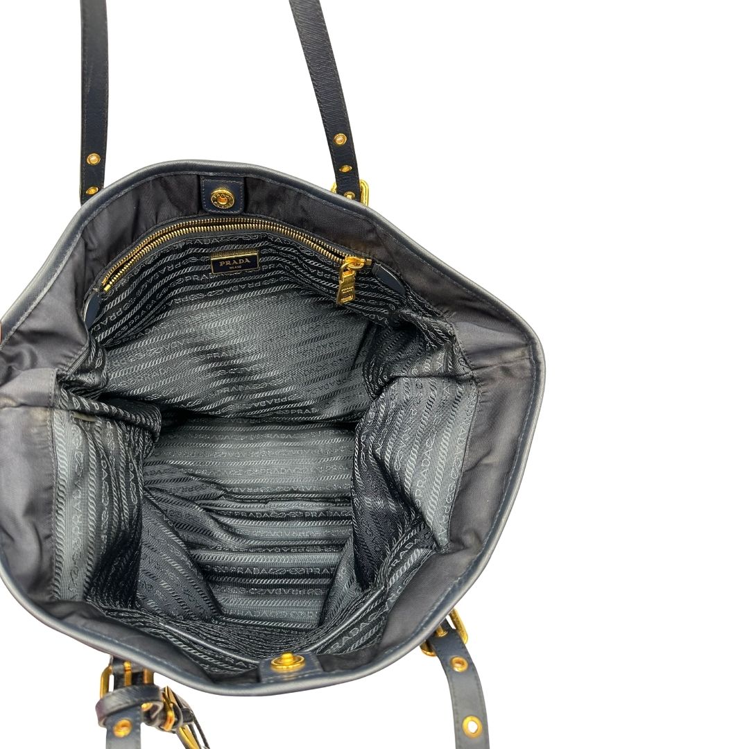 Interno di una borsa Prada in nylon blu navy e finiture in pelle saffiano tono su tono, con parti metalliche dorate; munita di un accessorio porta address e doppi manici leggermente regolabili. Indossabile a spalla. Completa di dustbag e card d'autenticità.