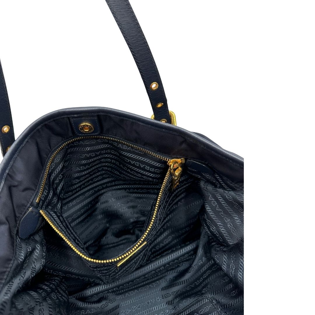 Interno di una borsa Prada in nylon blu navy e finiture in pelle saffiano tono su tono, con parti metalliche dorate; munita di un accessorio porta address e doppi manici leggermente regolabili. Indossabile a spalla. Completa di dustbag e card d'autenticità.