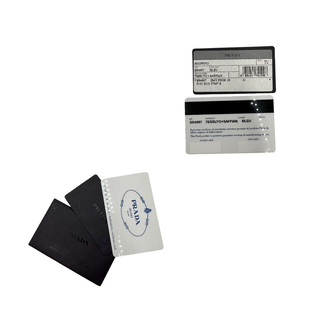Card d'autenticità di una borsa Prada in nylon blu navy e finiture in pelle saffiano tono su tono, con parti metalliche dorate; munita di un accessorio porta address e doppi manici leggermente regolabili. Indossabile a spalla. Completa di dustbag.