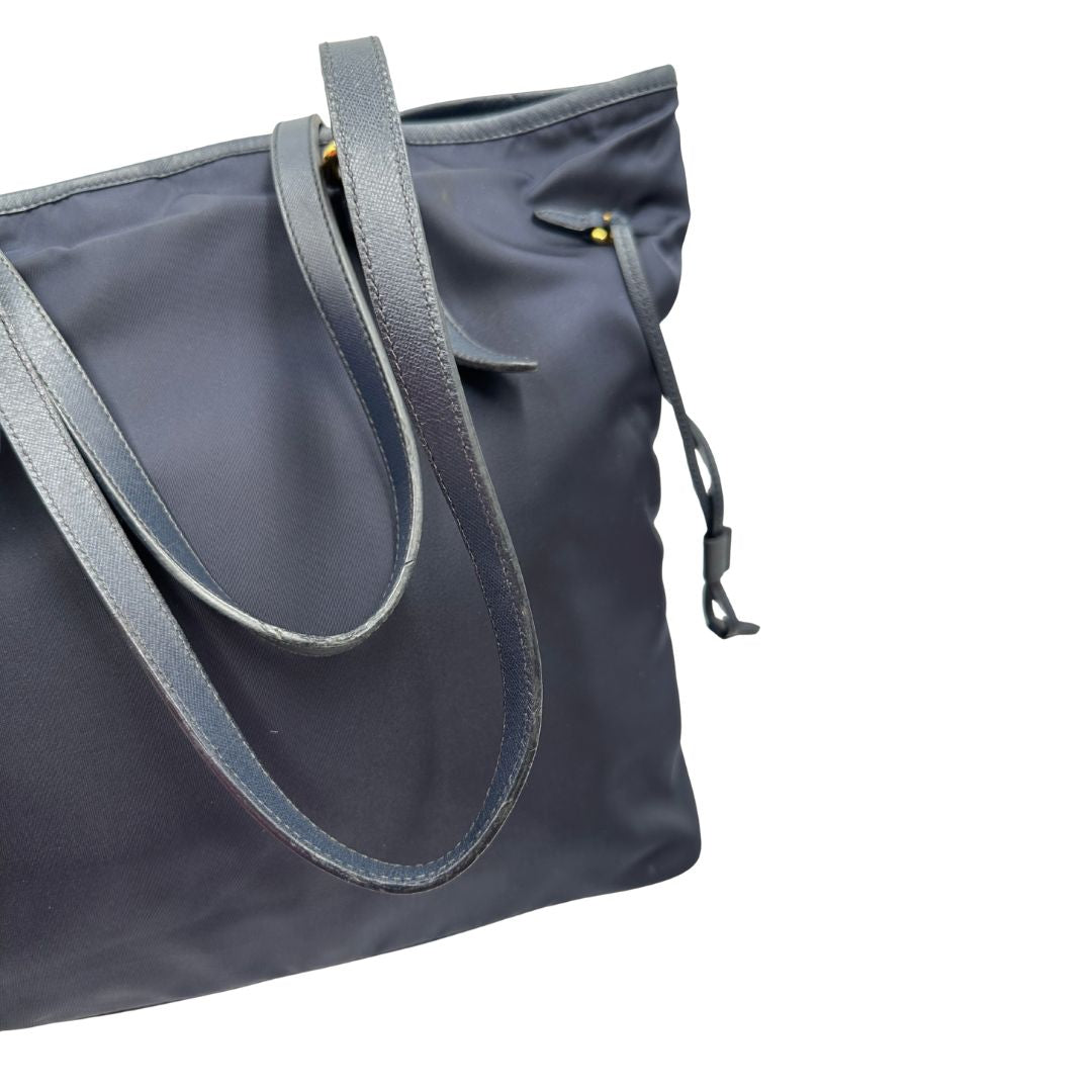 Difetto manici di una borsa Prada in nylon blu navy e finiture in pelle saffiano tono su tono, con parti metalliche dorate; munita di un accessorio porta address e doppi manici leggermente regolabili. Indossabile a spalla. Completa di dustbag e card d'autenticità.