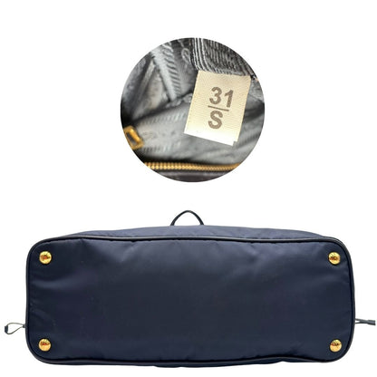 Base e codice di una borsa Prada in nylon blu navy e finiture in pelle saffiano tono su tono, con parti metalliche dorate; munita di un accessorio porta address e doppi manici leggermente regolabili. Indossabile a spalla. Completa di dustbag e card d'autenticità.