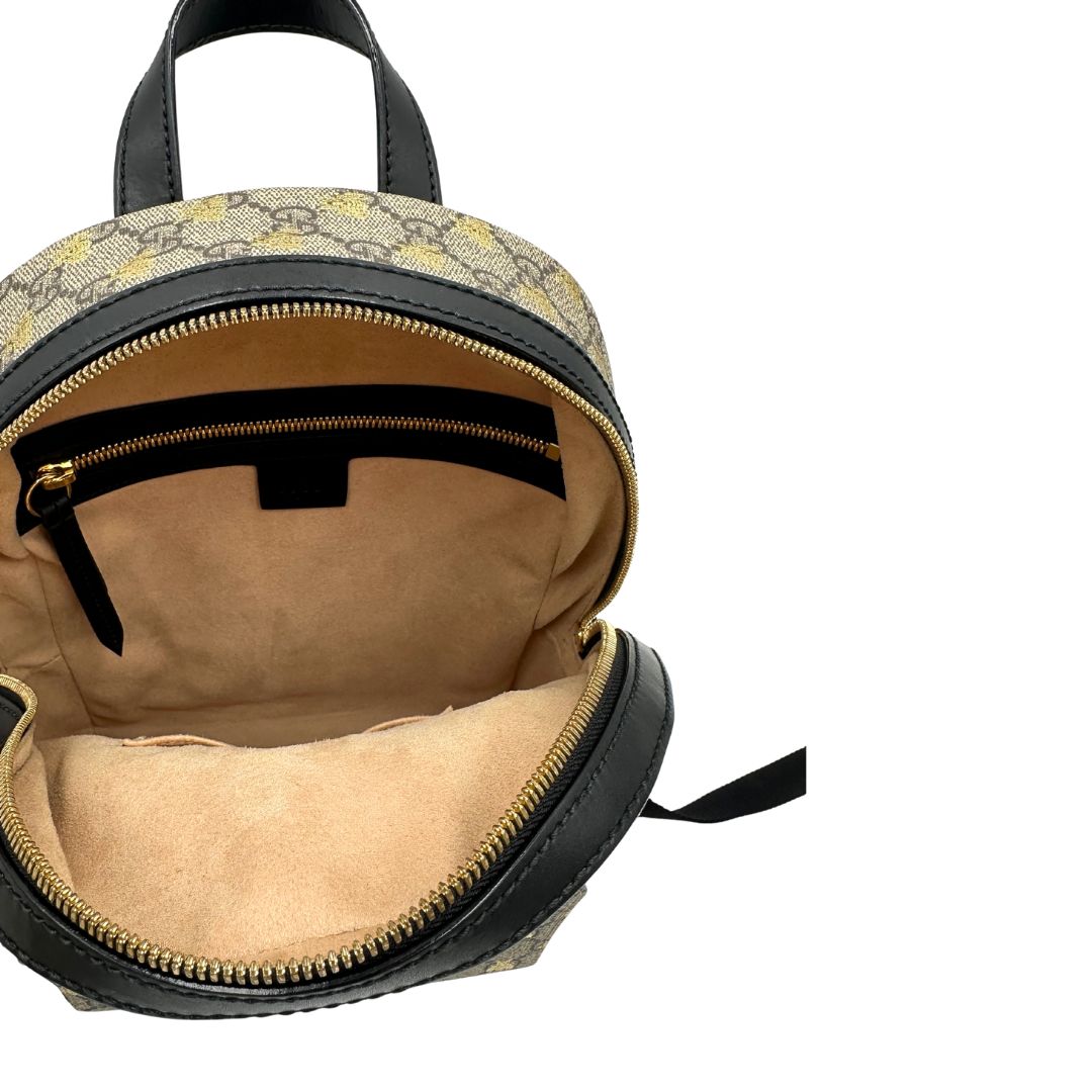 Interno di un Zaino Gucci in canvas GG beige con finiture in pelle nere e parti metalliche dorate; presenta una stampa di api dorate su tutta la superficie, munito di un manico e bretelle in tessuto regolabili. Originale, usato, di lusso, in ottime condizioni.