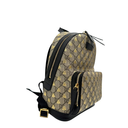 Lato destro di un Zaino Gucci in canvas GG beige con finiture in pelle nere e parti metalliche dorate; presenta una stampa di api dorate su tutta la superficie, munito di un manico e bretelle in tessuto regolabili. Originale, usato, di lusso, in ottime condizioni.