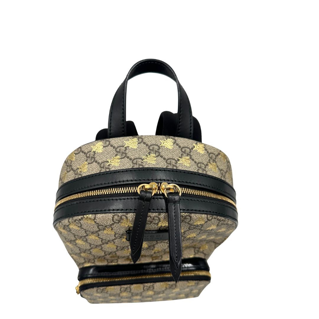 Chiusura di un Zaino Gucci in canvas GG beige con finiture in pelle nere e parti metalliche dorate; presenta una stampa di api dorate su tutta la superficie, munito di un manico e bretelle in tessuto regolabili. Originale, usato, di lusso, in ottime condizioni.