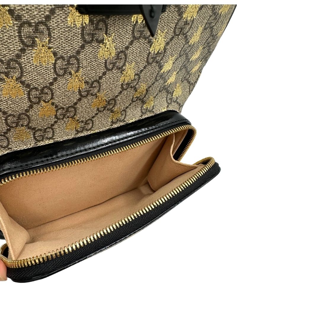 Tasca esterna di un Zaino Gucci in canvas GG beige con finiture in pelle nere e parti metalliche dorate; presenta una stampa di api dorate su tutta la superficie, munito di un manico e bretelle in tessuto regolabili. Originale, usato, di lusso, in ottime condizioni.