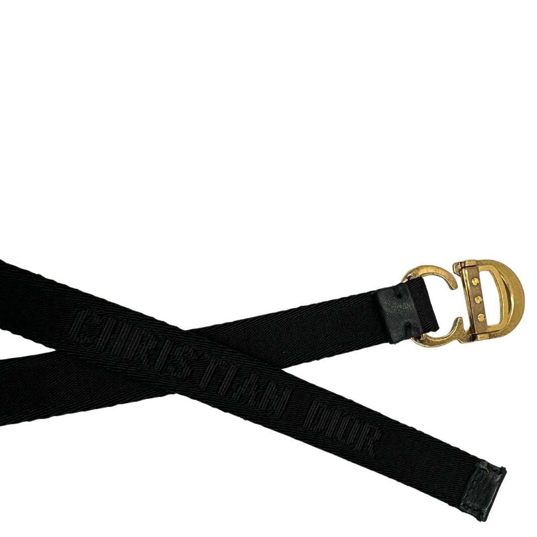 Cintura Christian Dior in tessuto logato nera, impreziosita da fibbia con CD in metallo dorato. Completa di dustbag. Chiusura a cricchetto.