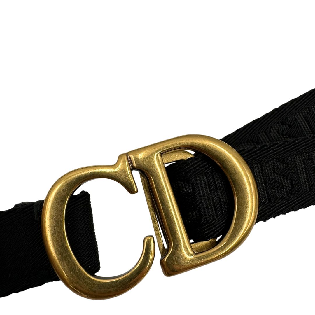 Cintura Christian Dior in tessuto logato nera, impreziosita da fibbia con CD in metallo dorato. Completa di dustbag. Chiusura a cricchetto.